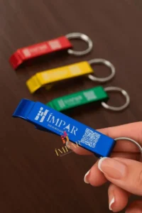 Close-up de uma mão usando o chaveiro abridor para levantar o anel de uma lata de alumínio, protegendo a unha de quem o utiliza.